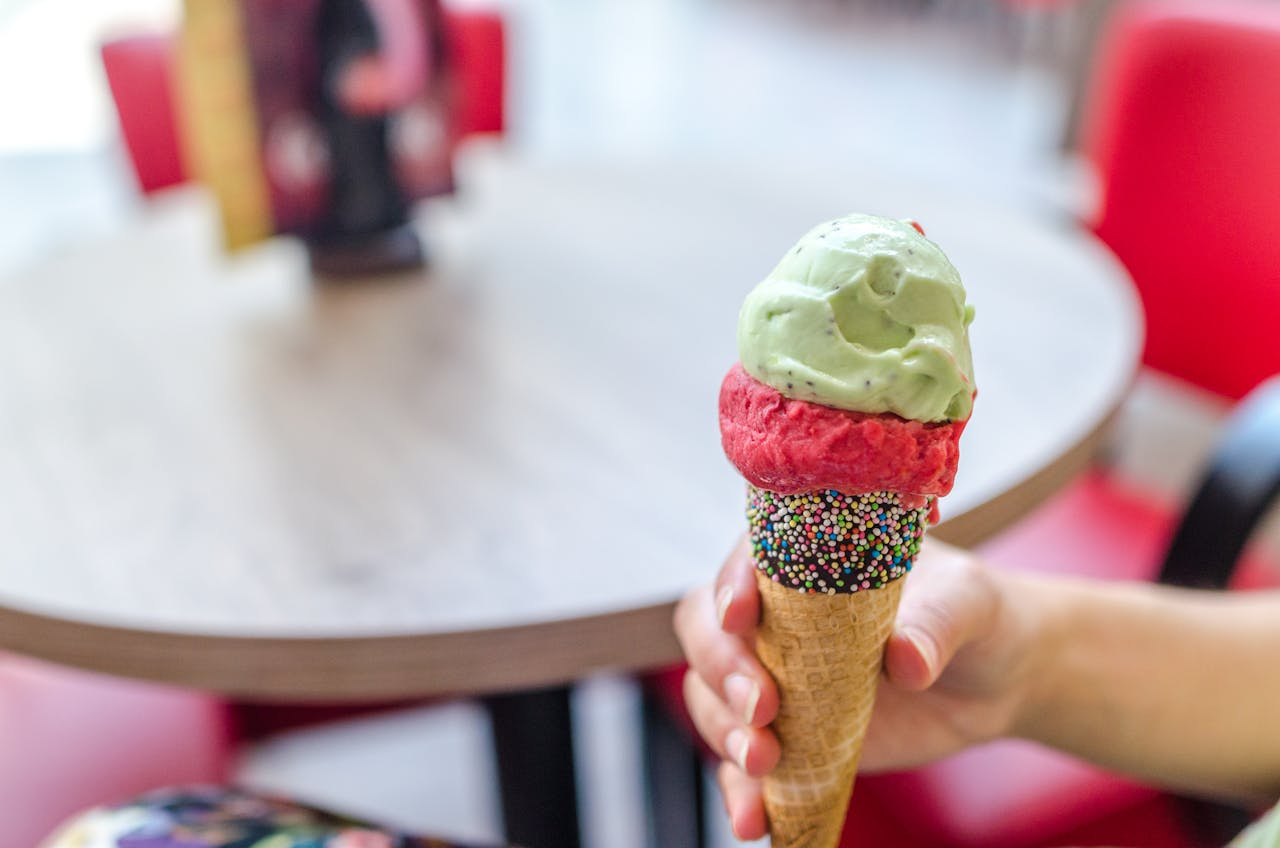 project-01-c Hand holding a colorful ice cream cone topped with mint and raspberry scoops indoors.