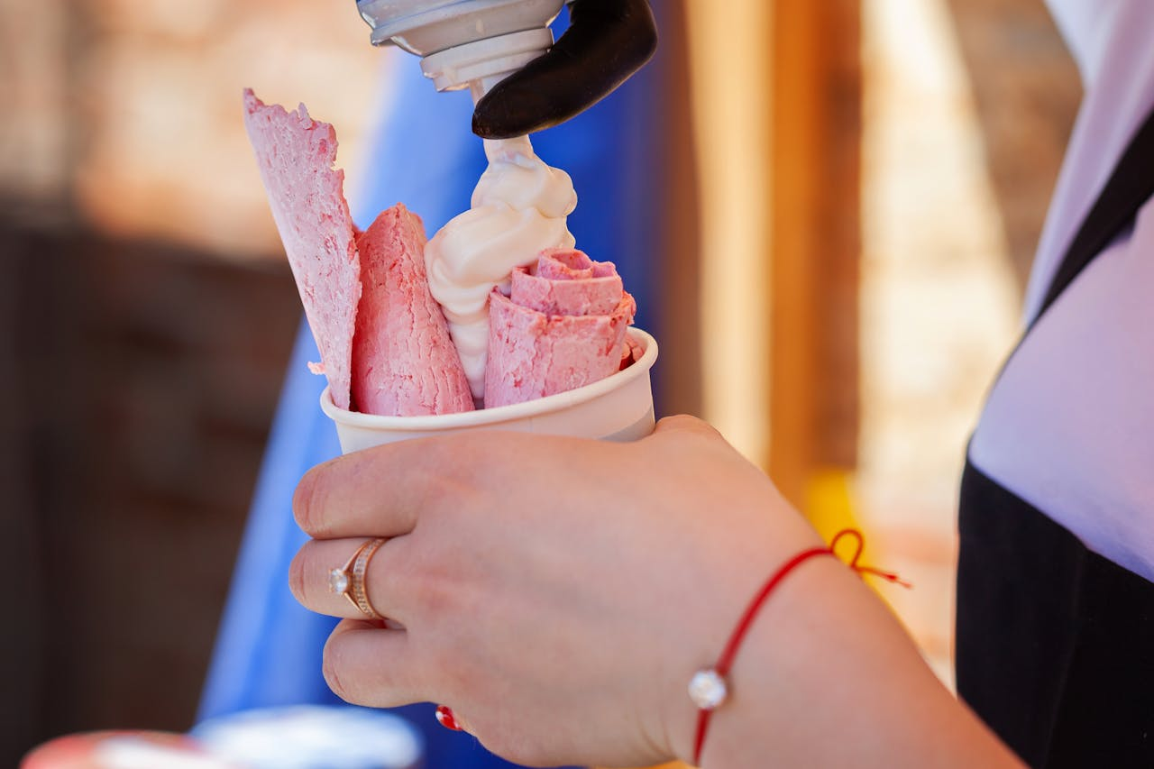 Delicious rolled ice cream being topped with soft cream, held by a person with jewelry.